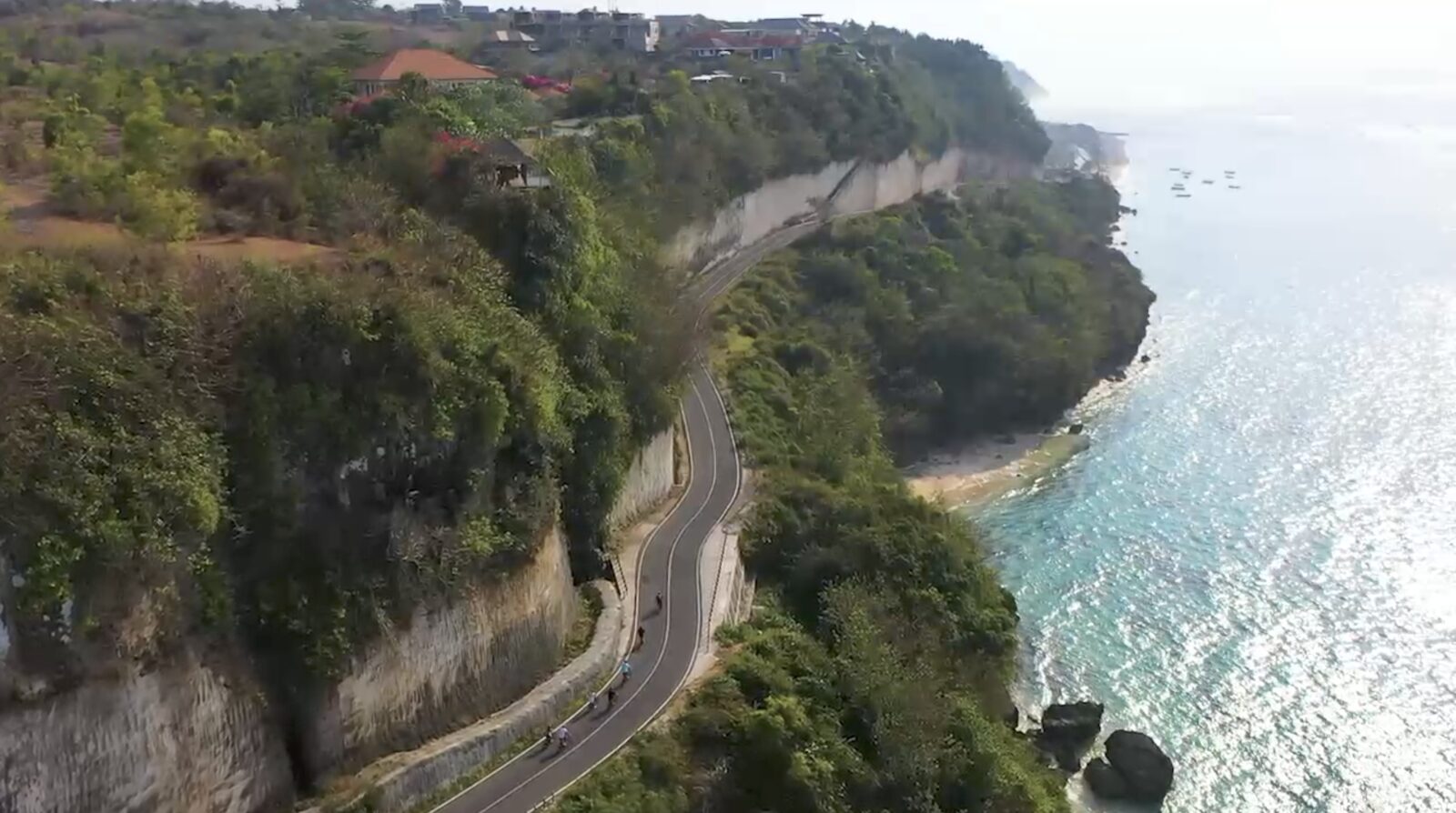Cyclists riding e-bikes along a dramatic Bali coastal cliff road above turquoise ocean โ UNIKAT E-Bike Tours